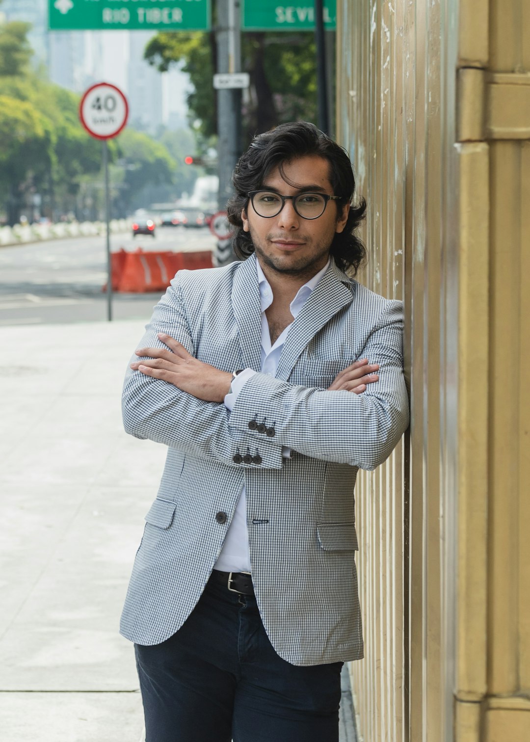 A man in a suit leans against a wall outdoors.